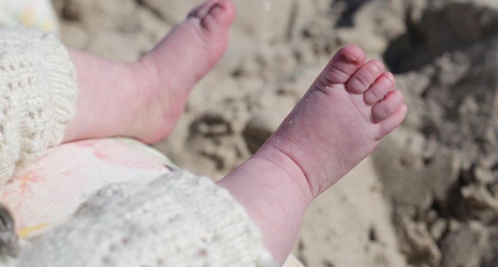 Babyfüße ohne Schuhe und Socken am Strand.