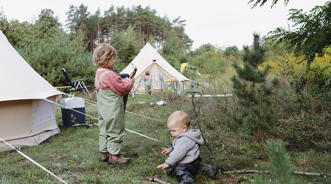 Kinder spielen neben dem Zelt mit Stöckern aus der Natur.