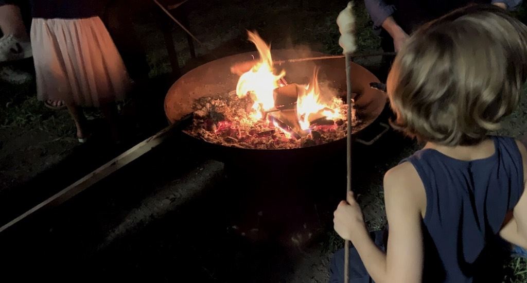 Ein Kind steht mit Stockbrot in der Hand am Feuer.