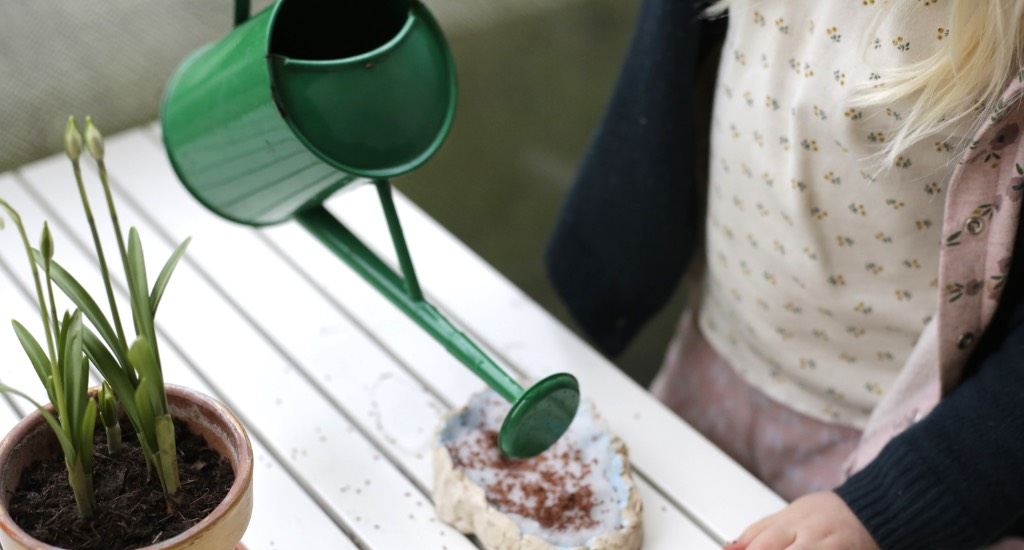 Kind gießt mit grüner Gießkanne Samenkörner.