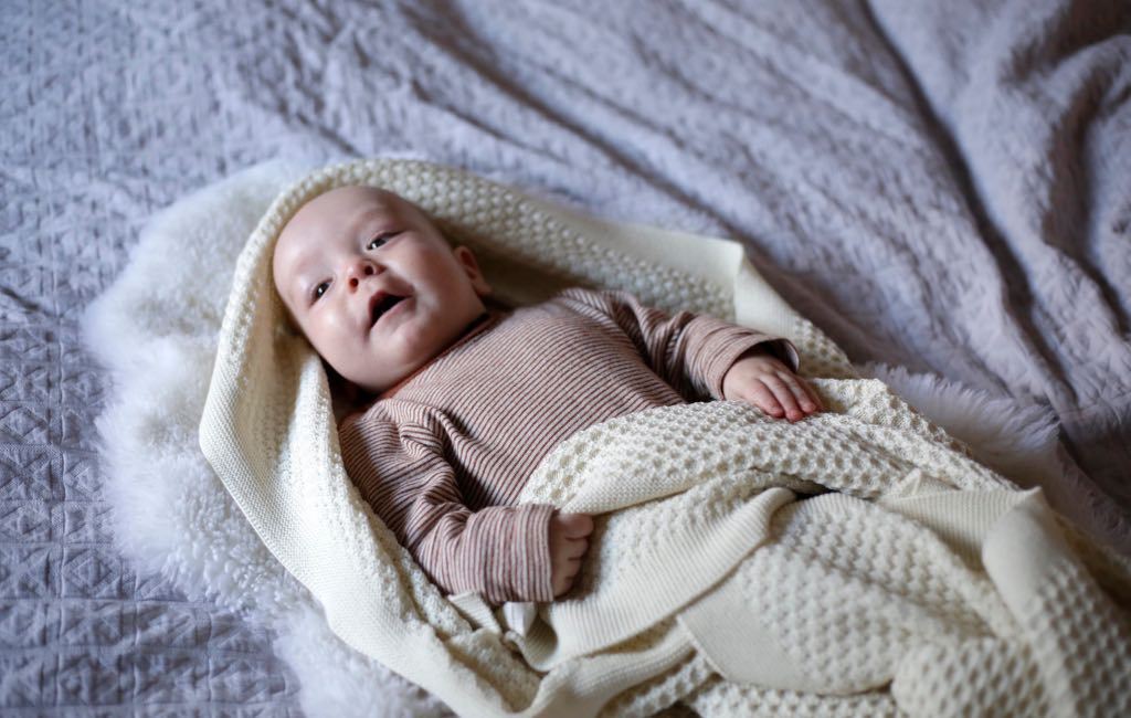 Ein Baby liegt eingewickelt in eine kuschelige Wolldecke.